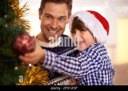 Ich bin in festlicher Stimmung. Ein kleiner Junge, der den Weihnachtsbaum mit seinem Vater schmückt. Stockfoto