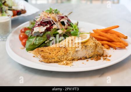 Gegrilltes Seebarschsteak mit Kräuterkruste und Gemüse auf einem weißen Teller Stockfoto