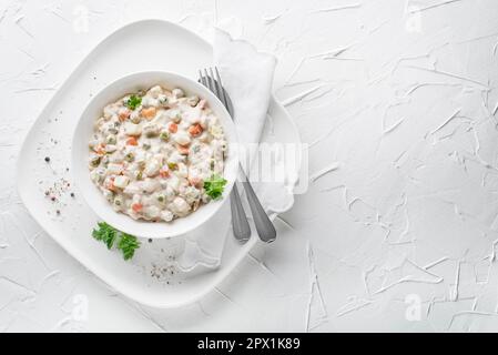 Schüssel mit russischem Salat olivier französischer Salat mit Gemüse und Ei mit Mayonnaise auf weißem Tisch Stockfoto