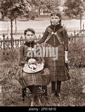 1890S 1900S PORTRÄT VON ZWEI JUNGEN MÄDCHEN, DIE DAZU PASSENDE KAROTTEN TRAGEN, EIN STEHENDES MÄDCHEN, DAS MIT EINEM HUT AUF IHR SITZT RUNDE - O2953 HAR001 HARS FREUNDSCHAFT DURCHGEHEND DURCHDACHTE INSPIRATION TEENAGER MÄDCHEN KARO GESCHWISTER SELBSTVERTRAUEN SCHWESTERN 1800S B&W SCHOSSKLEIDER PASSEND STOLZ AUS DEM 20TH. JAHRHUNDERT GESCHWISTERVERBINDUNG AUS DEM 19TH. JAHRHUNDERT STYLING AUFRICHTIG GEKLEIDET, GLEICHERMASSEN FOKUSSIERTE, INTENSIVE JUGENDLICHE KINDER IM ALTER VON JUGENDLICHEN MÄDCHEN-ZUSAMMENSEIN SCHWARZ-WEISS VORSICHTIG WEISSE ETHNISCHE ZUGEHÖRIGKEIT ERNST HAR001 INTENTION ALTMODISCH Stockfoto