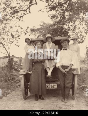 1910S MANN UND FRAU STEHEN VOR DEM AUTO, DREI FRAUEN POSIERTEN UND STANDEN AUF DEM AUTO UND SCHAUTEN ALLE ZU VOR DER KAMERA - O3981 HAR001 HARS-BRÜDER LÄNDLICHER EHEPARTNER ERWEITERTE EHEMÄNNER KOPIEREN WELTRAUMFREUNDSCHAFT VOLLE LÄNGE, HALBE LÄNGE, FRAUEN, AUTO, MÄNNER GESCHWISTER SCHWESTERN TRANSPORT B&W PARTNER BLICKKONTAKT ADVENTURE AUTOS STOLZ GESCHWISTER VERBINDUNG AUTOS STILVOLLE FAHRZEUGE VOR KOOPERATION MITTE ERWACHSENER MITTELERWACHSENER MANN MITTELERWACHSENE FRAU POSIERTE ZUSAMMENSEIN EHEFRAUEN JUNGE ERWACHSENE FRAU SCHWARZ-WEISS WEISSE ETHNISCHE ZUGEHÖRIGKEIT HAR001 HUMORLOS ALTMODISCH Stockfoto