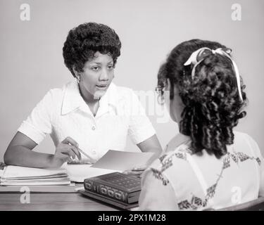 1970S AFROAMERIKANERIN LEHRERBERATUNG IM GESPRÄCH MIT TEENAGER HIGH SCHOOL SCHÜLERIN VON HINTEN GESEHEN - S20375 HAR001 HARS FUTURE NOSTALGIE ALTE MODE 1 JUGENDLICHE LEHRER KOMMUNIKATION KARRIERE TEAMWORK INFORMATIONEN LIFESTYLE BERATER FRAUEN JOBS STUDIO AUFNAHME COPY SPACE HALBE LÄNGE DAMEN PERSONEN INSPIRATION TEENAGER MÄDCHEN BERUF B&W SCHULEN BERATUNG FÄHIGKEITEN BERUF KOPF UND SCHULTERN AFROAMERIKANER AFROAMERIKANER NETWORKING KARRIERELEHRER PROGRESS BLACK ETHNICITY PRIDE OPPORTUNITY AUTHORITY HIGH SCHOOL JOBS HIGH SCHOOLS CONNECTION PÄDAGOGE Stockfoto