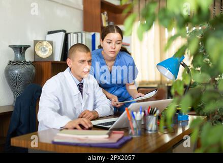 Junge Kollegen-Ärzte diskutieren die Verabredung der Behandlung, sitzen am Computer im Büro Stockfoto