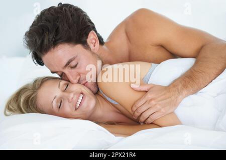 Süßer Morgen geküsst. Ein Ehemann umarmt seine Frau und küsst sie liebevoll auf die Wange, während sie morgens aufwacht. Stockfoto