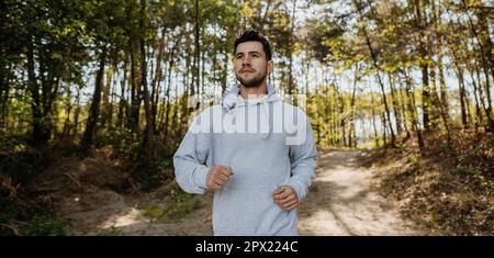 Portrait eines Jogging-Fitnessmodells für Männer beim Training auf der Waldstraße in der Naturlandschaft. Stockfoto