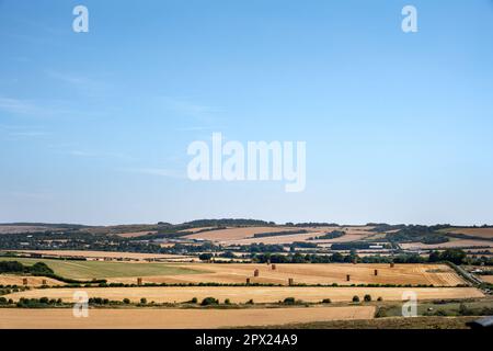Blick auf die Landschaft in Wiltshire, die Getreidefelder und die gestapelten Strohballen an einem sonnigen Sommernachmittag in Südwestengland Stockfoto