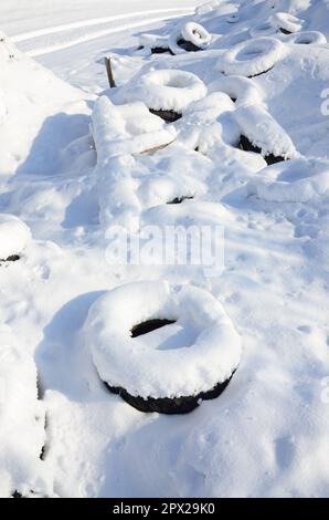 Gebrauchte und entsorgte Autoreifen liegen am Straßenrand und sind mit einer dicken Schneeschicht bedeckt Stockfoto