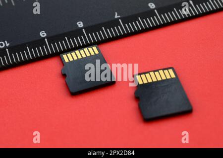 Zwei kleine microSD-Speicherkarten liegen auf rotem Hintergrund neben einem schwarzen Lineal. Ein kleiner und kompakter Daten- und Informationsspeicher Stockfoto