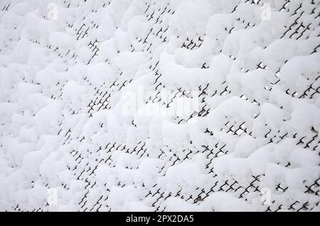 Nahaufnahme aus Metallgitter, bedeckt mit einer dicken Schicht Schnee in den Zellen Stockfoto