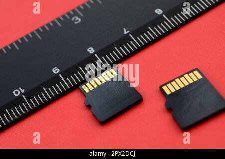 Zwei kleine microSD-Speicherkarten liegen auf rotem Hintergrund neben einem schwarzen Lineal. Ein kleiner und kompakter Daten- und Informationsspeicher Stockfoto