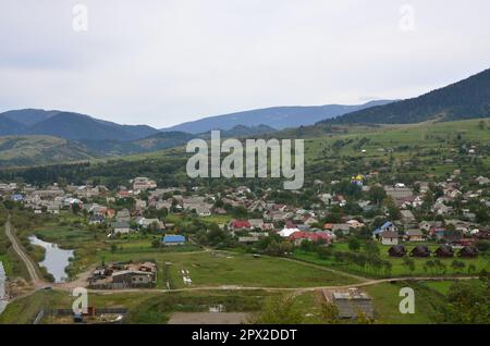 Eine wunderschöne Aussicht auf das Dorf Mezhgorye, Karpaten Region. Eine Menge von Wohngebäuden durch hohe Wald Berge und lange Fluss umgeben Stockfoto