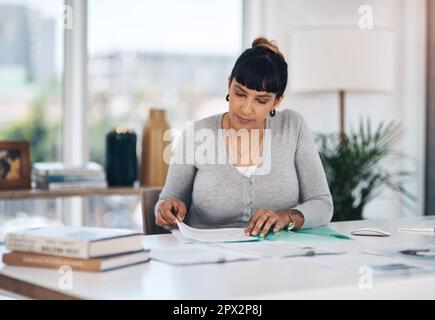 Dateien werden aktualisiert. Eine attraktive junge Geschäftsfrau, die allein in ihrem Büro sitzt und sich den Papierkram durchliest Stockfoto