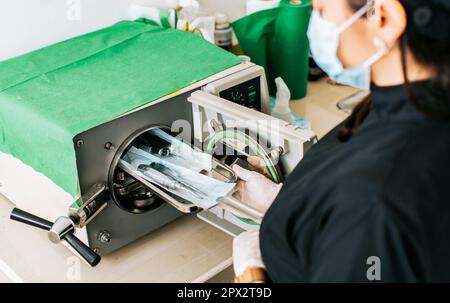 Ein Zahnarzt, der seine Werkzeuge sterilisiert, ein Zahnarzt mit einem Zahnsterilisator, Ein Zahnarzt mit einem Zahnautoklav, Nahaufnahme eines Zahnarztes mit einem Dampfsterilisator Stockfoto