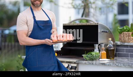 Grillen Sie Lachsfisch beim Mann tragen Sie eine Schürze mit Aussicht Stockfoto