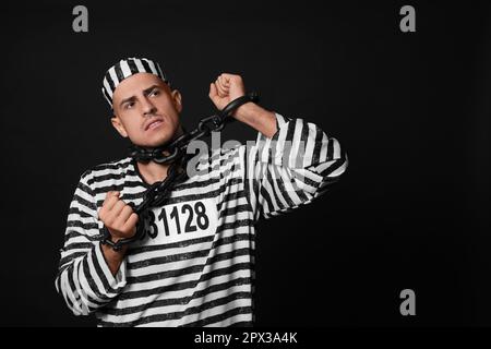 Gefangener in gestreifter Uniform mit angeketteten Händen auf schwarzem Hintergrund Stockfoto