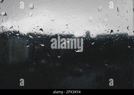 Schlechtes Wetter in der Stadt. Gebäude, Häuser, Autos vor dem Fenster. Wolkenbewölkung. Meteorologie und Wettervorhersage. Heruntergekommene Regentropfen Stockfoto