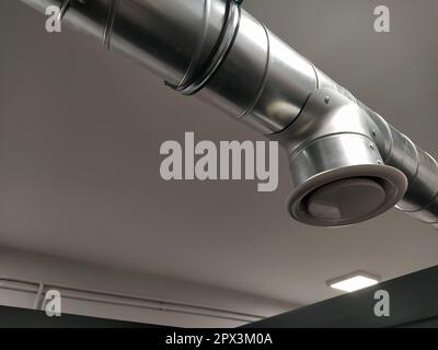 Abzugshaube in einer öffentlichen Toilette. Rundes Metallrohr mit grauem Luftabsauger. Technische Lüftungssysteme. Verzinkte Rohre unter der Decke von Th Stockfoto
