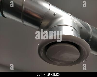 Abzugshaube in einer öffentlichen Toilette. Rundes Metallrohr mit grauem Luftabsauger. Technische Lüftungssysteme. Verzinkte Rohre unter der Decke von Th Stockfoto