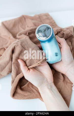 Ein Mädchen entfernt große Spulen aus der Kleidung mit einer elektronischen Maschine. Das Konzept der Kleiderschonung, Spulenreinigung Stockfoto