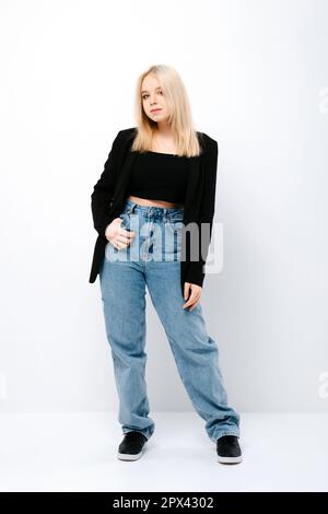 Blondes Mädchen mit schwarzem Oberteil, Jacke und Jeans posieren Stockfoto