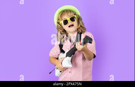 Porträt eines kleinen Jungen mit rosa Sonnenbrille, der elektrische Gitarre spielt. Der süße Junge singt und spielt mit hellen Emotionen auf der E-Gitarre. Stockfoto