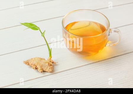 Frisch gelb heißen Tee gebraut, chemische Ingwerwurzel mit grünen Frühling Neben es auf White boards Schreibtisch Stockfoto