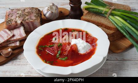 Traditioneller ukrainischer Borschtsch . Weiße Platte aus Rote-Beete-Wurzel-Suppe Borsch mit weißer Sahne, grünen Zwiebeln, gesalzenem Schweineschmalz (salo). Rübenwurzel-Feinkost Stockfoto