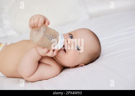 Charming Baby Mädchen liegt im Bett und trinkt Wasser aus einer Flasche Stockfoto