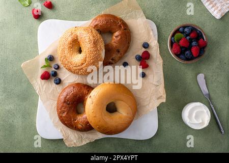 Hausgemachte, frisch gebackene Bagels auf Pergamentpapier, verzehrfertig, Zimtrosinen, Sesam und Bagel mit Frischkäse und frischen Beeren Stockfoto