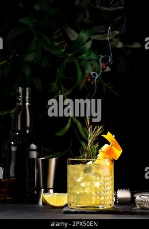 Penicillin-Cocktailgetränk mit Scotch, Whiskey, Sirup, Zitronensaft und Eis in Glas mit Orangenschale, garniert mit dampfendem Rosmarin. Schwarzer Backgro Stockfoto