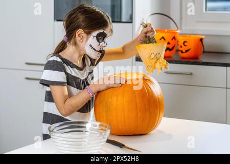 Junges Mädchen mit Totenkopf Gesichtsfarbe schneiden einen Kürbis in ihrer Küche. Stockfoto