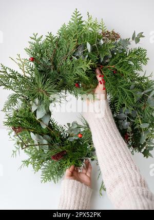 Stilvoller Weihnachtskranz für den Innenraum, hängen Sie den Kranz an die Tür. Handgemacht, hält das Mädchen einen frisch gemachten Kranz in der Hand. Die Atmosphäre von Stockfoto