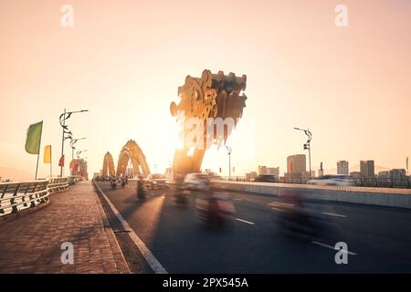 Verkehr mit vielen Motorrädern in unscharfer Bewegung auf der Dragon Bridge. Da Nang Stadt bei goldenem Sonnenuntergang, Vietnam. Stockfoto