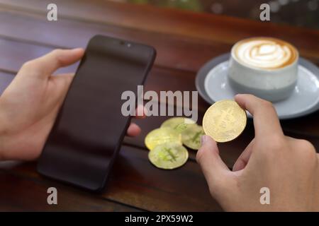 Nahaufnahme von männlicher Hand mit Bitcoin und leerem Bildschirm Telefon. Das Konzept des Kryptowährungshandels Stockfoto