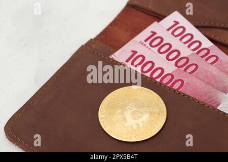 Bitcoin mit 100.000 Rupiah-Banknote auf Ledergeldbörse. Das Konzept des Kryptowährungshandels Stockfoto