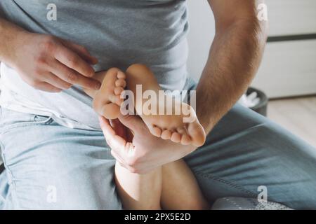 Kinderfüße in den Händen des Vaters. Papa kitzelt die Füße des Kindes, das auf ihnen sitzt. Familie, die Spaß zu Hause hat Stockfoto