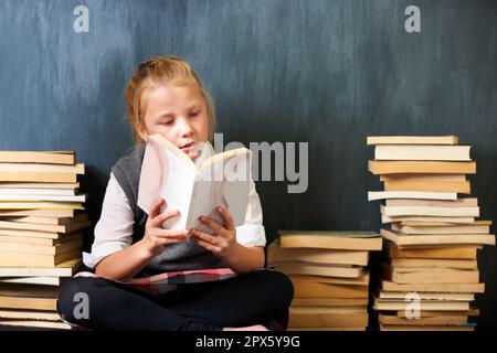 Ein paar Studien nachholen. Ein süßes blondes Mädchen, das im Unterricht liest, umgeben von Büchern. Stockfoto