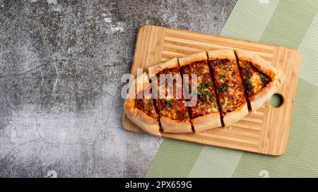 Geschnittene Pide (türkische Pizza oder Pita-Gericht) mit Rinderhack, Käse, Tomaten und Gemüse auf einem rechteckigen Holzbrett mit dunkelgrauem Hintergrund Stockfoto