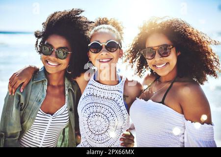 Wir lieben es, dass wir den Sommer zusammen verbringen können. Drei Freunde amüsieren sich an einem sonnigen Tag am Strand Stockfoto