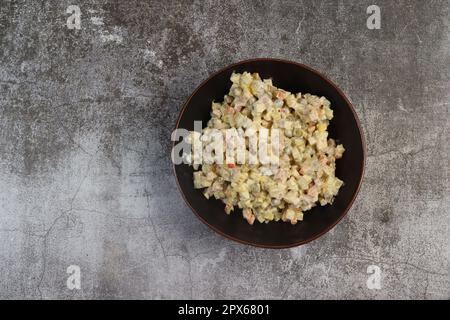 Hausgemachter russischer Salat oder Olivier aus gekochtem Gemüse und Wurst in einer Schüssel auf dunklem Hintergrund. Draufsicht, flach liegend Stockfoto