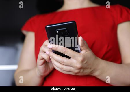 Frau in rotem Kleid mit Smartphone, Mobiltelefon in weiblichen Händen nah dran. Konzept der Online-sucht, sms, soziale Medien Stockfoto