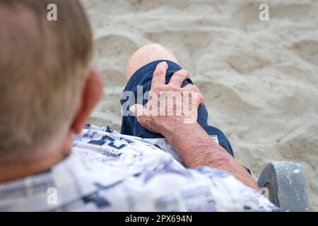 Älterer Mann mit der Hand auf dem Schoß. Nahaufnahme der Haut mit Flecken und Falten, Alterungskonzept. Stockfoto