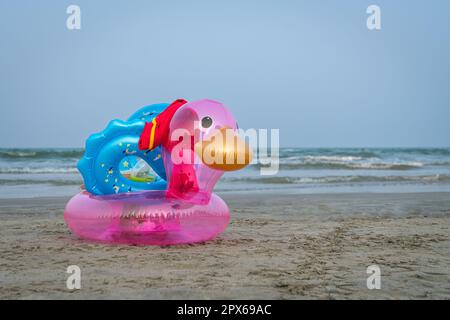 Aufblasbare Ente an einem Sandstrand. Meer und blauer Himmel im Hintergrund. Sommerurlaub und Urlaubskonzept. Stockfoto