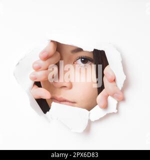 Junge asiatische Frau reißen Loch in der Wand zu Peek durch Stockfoto