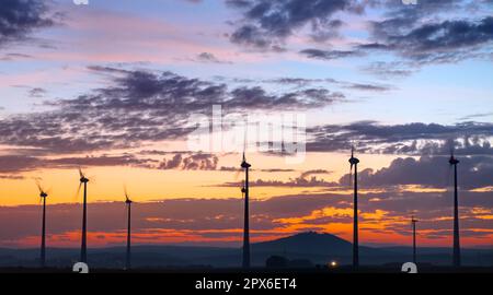 Drehende Windturbinen vor einem Sonnenuntergang in Deutschland Stockfoto