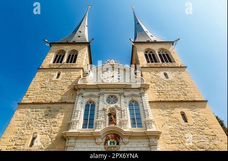 Froschperspektive auf die Vorderseite der Kirche des katholischen Hofs St. Leodegar in Luzern mit seinen zwei Türmen und einer Uhr mit Uhr in der Sonne Stockfoto