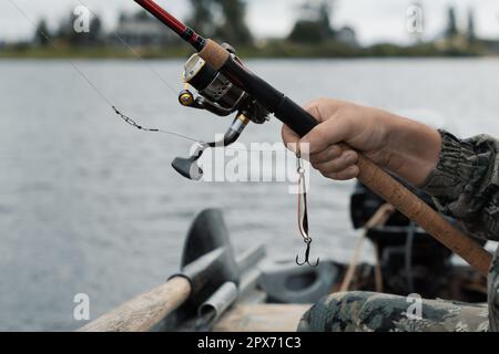 Ein Fischer hält eine Drehstange mit Angelrolle und Angelköder in der Hand im Boot, aus nächster Nähe Stockfoto