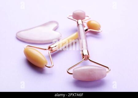 Gua-Sha-Stein und verschiedene Gesichtsrollen auf violettem Hintergrund Stockfoto