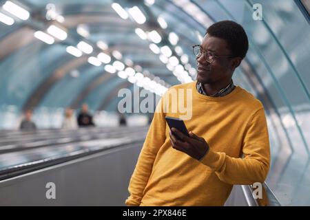 Afroamerikanischer junger Geschäftsmann, der sein Smartphone benutzt, während er auf einer Rolltreppe im Untergrund steht Stockfoto
