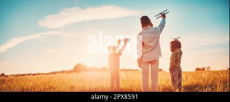 Vater und seine Kinder spielten mit dem Spielzeug des Flugzeugs auf dem Abendfeld. Konzept von Liebe und Familienurlaub. Stockfoto